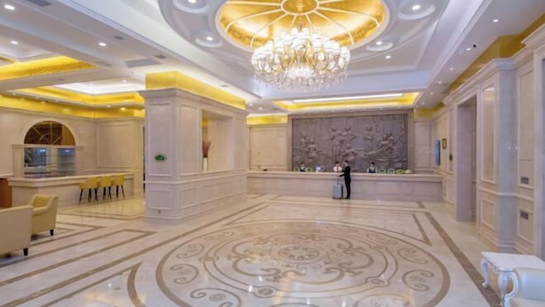 Un vestíbulo amplio con una gran araña, una mesa de recepción y un muro decorativo.