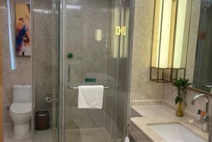 Un baño moderno con ducha envuelta en vidrio, inodoro, lavamanos con espejo y una planta en maceta.