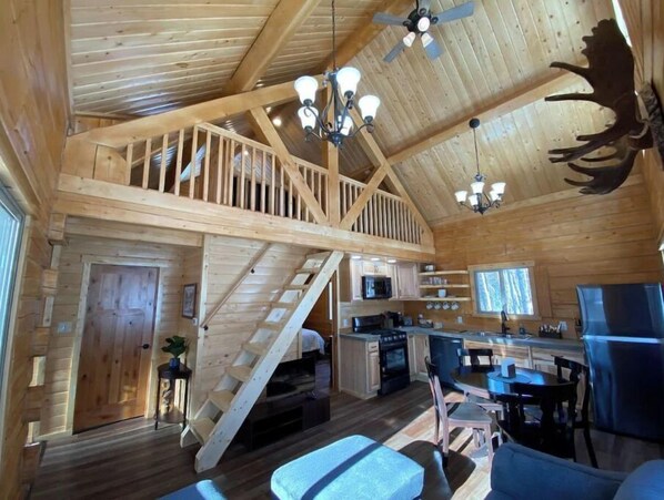 A cabin interior with a loft bedroom, kitchen, and dining area. - Beautiful Comfy Alaskan Log Home 2 (Wasilla)