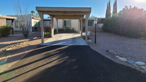 Un camino cubierto que lleva a una casa con el número 160, rodeada de jardines y un cielo despejado.