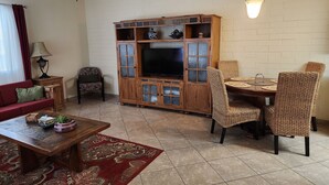 Un salón con televisor, aparador de madera, sofá rojo y sillas de mimbre.