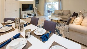 A modern living room with a dining area set for a meal, a sofa, and a TV in the background. - 3BR Townhouse with New Hot Tub - Near Disney! (Kissimmee)