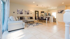 A modern living room with a sofa, coffee table, and dining area. There is a kitchen in the background with cabinets and a microwave. - 3BR Townhouse with New Hot Tub - Near Disney! (Kissimmee)