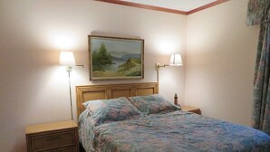 A bedroom with a bed, two bedside tables, a nightstand, a painting on the wall, and two lamps.