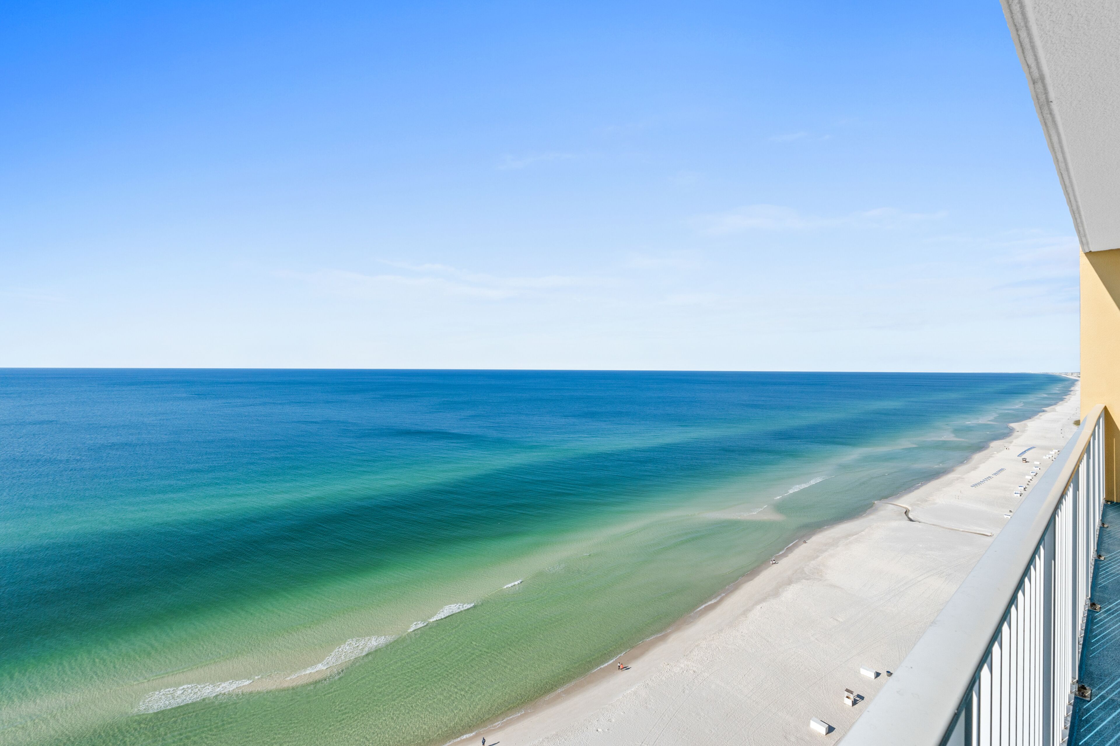 A beach view from a balcony with clear blue water and a sandy shore.