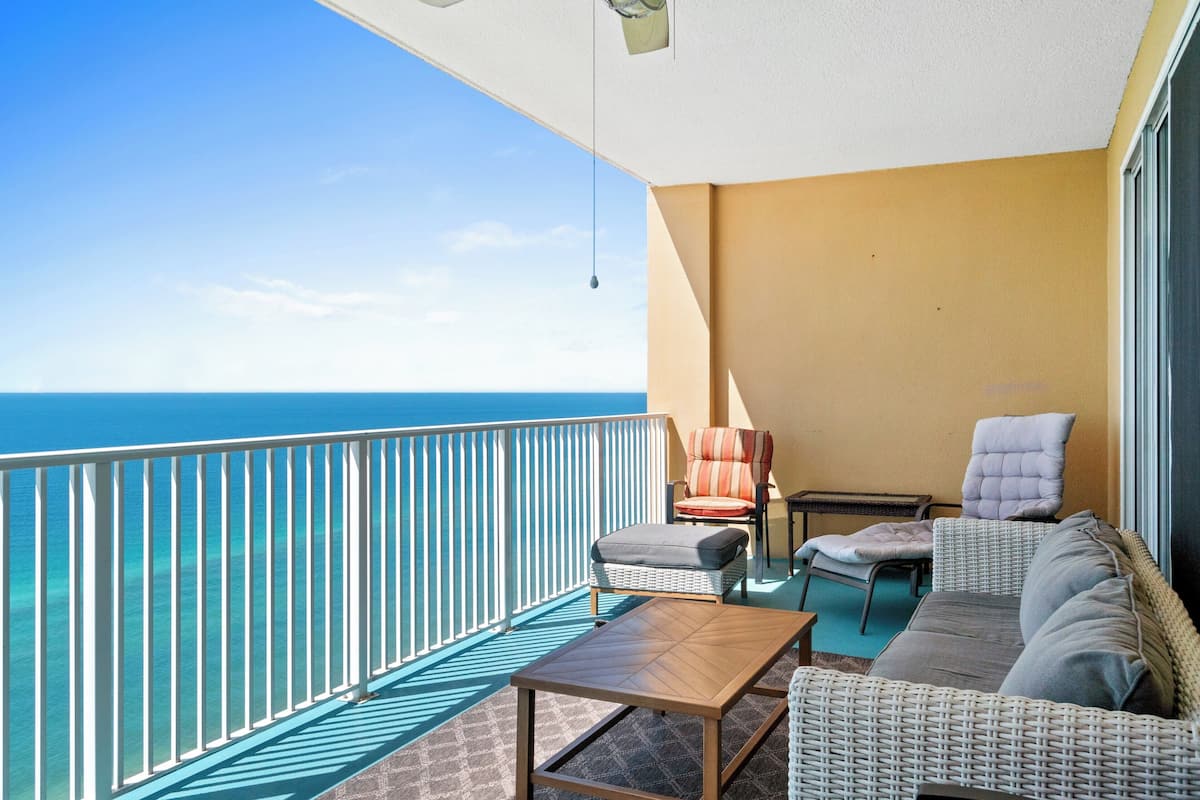 Een balkon met uitzicht op de oceaan, rieten meubilair en een hanglamp.