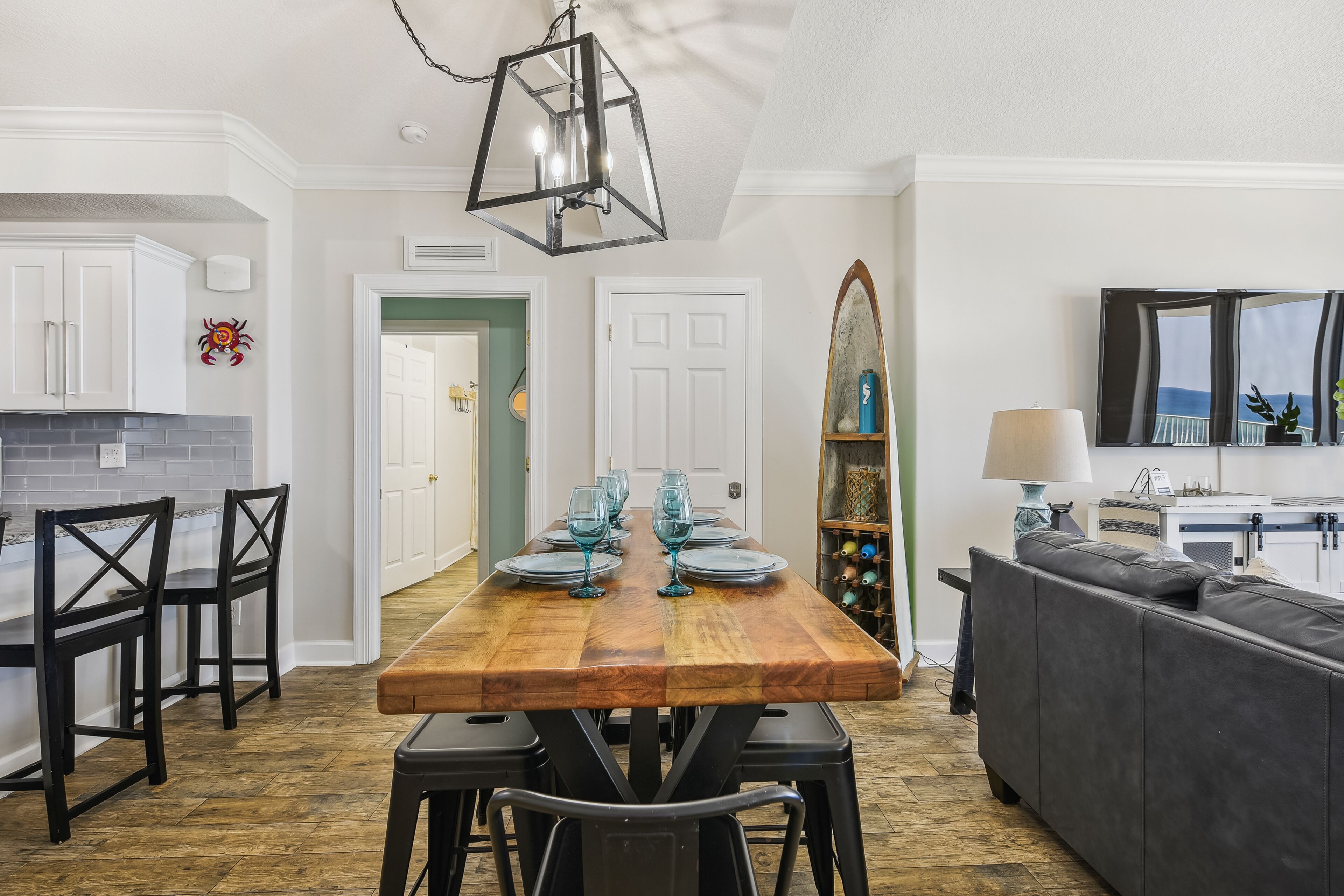 Un coin repas avec une table en bois dressée pour quatre personnes, un lustre noir et un canapé gris en arrière-plan.