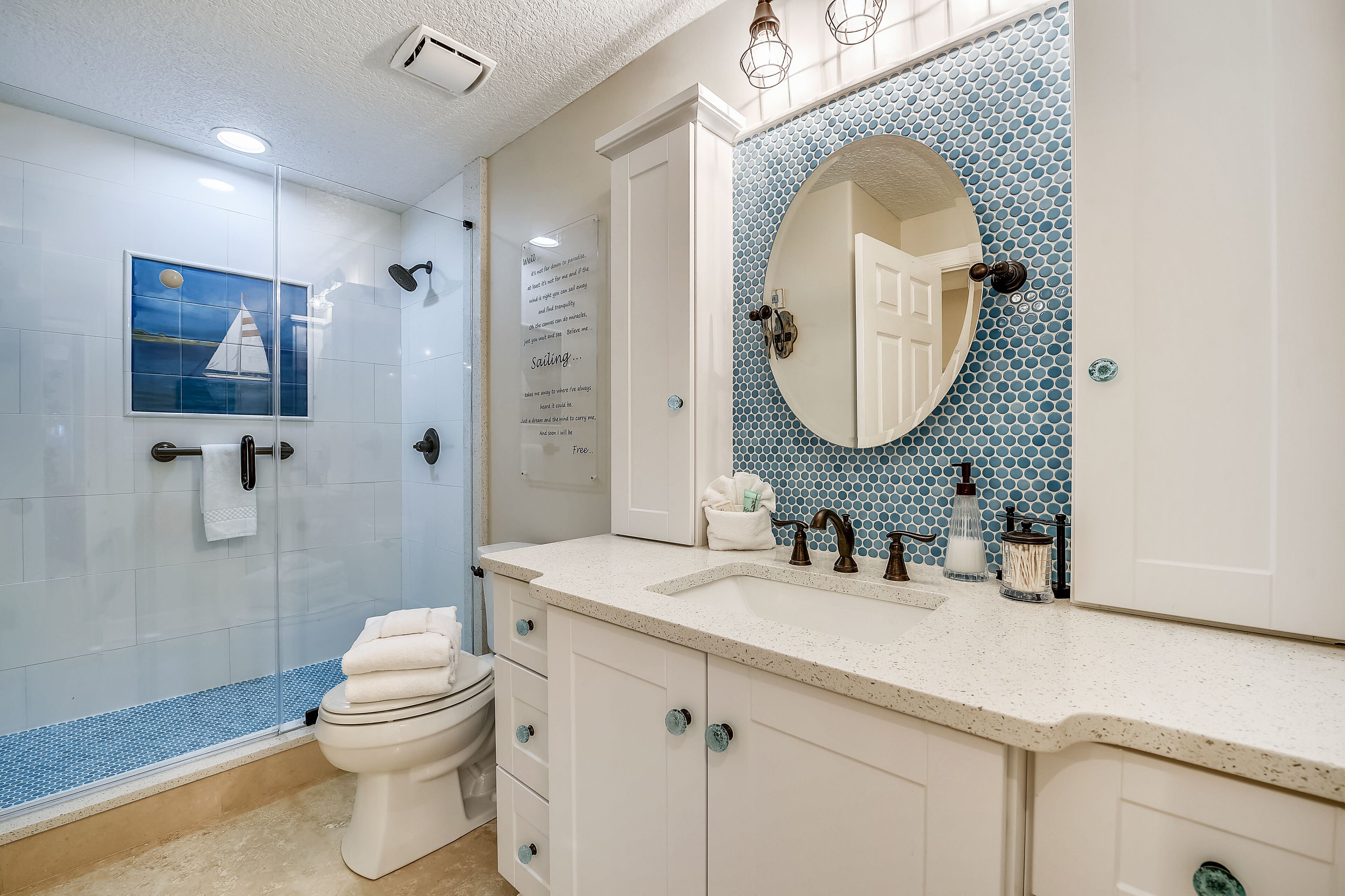 A bathroom with a glass shower enclosure, a toilet, a sink with a mirror, and a decorative tile backsplash.