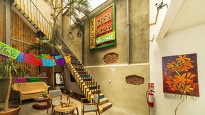 Un escalier aux marches colorées, un canapé en osier, une petite table ronde et une chaise. Un extincteur est fixé au mur.