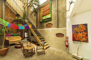 Un escalier aux marches colorées, un canapé en osier, une petite table ronde et une chaise. Un extincteur est fixé au mur.