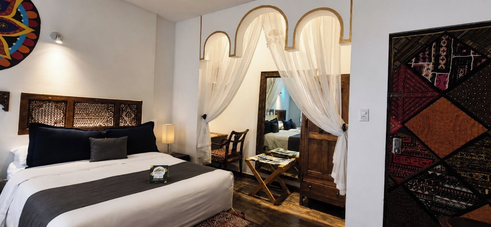 Une chambre d’hôtel comprenant un lit, une table de chevet, une chaise, un bureau en bois et un miroir.