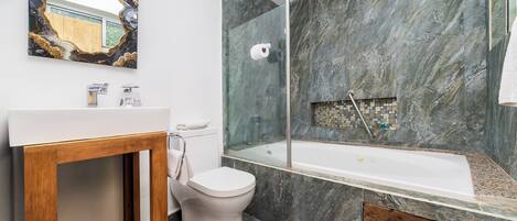 Un baño moderno con ducha de mármol, inodoro con mampara de vidrio y tocador de madera.