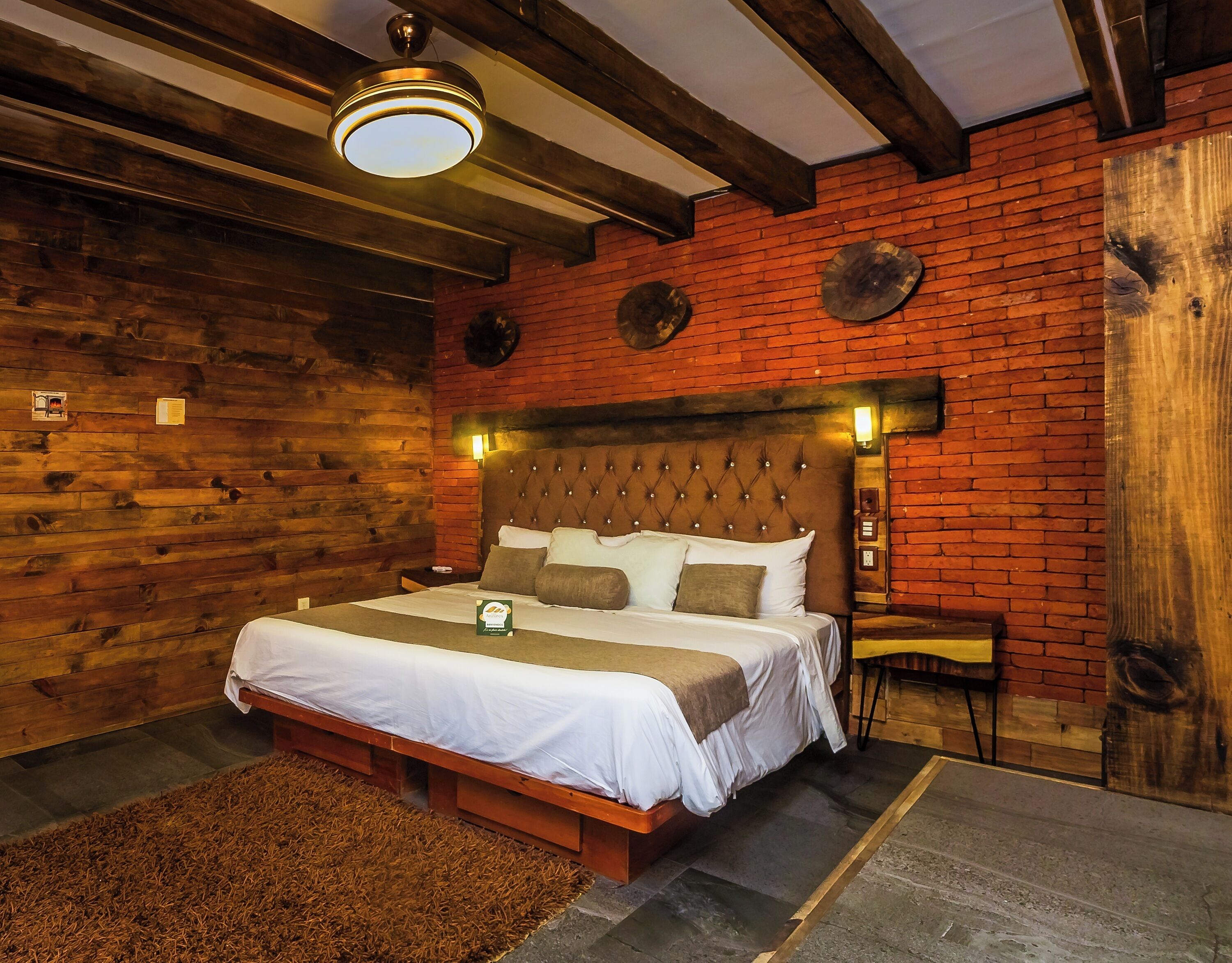 A wooden room with a large bed, a nightstand, and a wall-mounted heater.