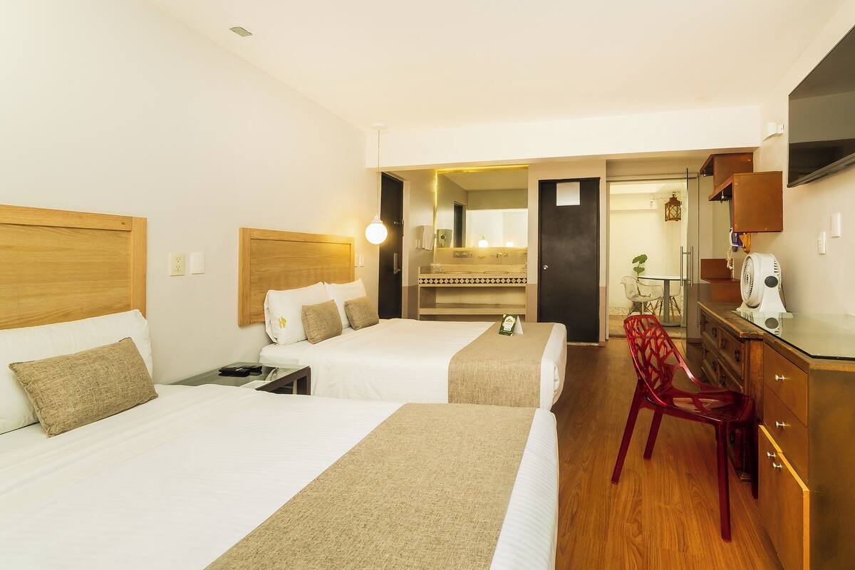 A hotel room with two beds, a desk, a chair, a mirror, and a dresser.