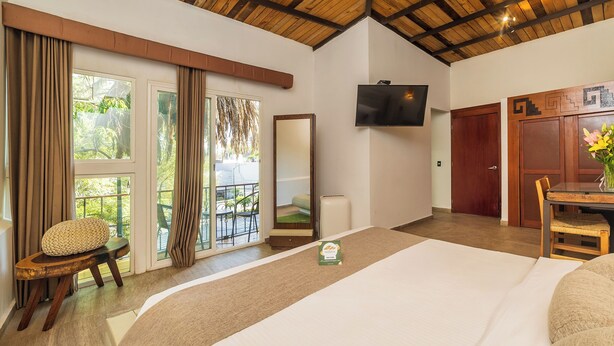 Une chambre d’hôtel dotée d’un grand lit, d’un plafond en bois, d’une télévision, d’un balcon avec vue et d’un coin repas comprenant une table et des chaises.