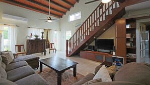 Un salón amplio con techo alto, una escalera de madera y un televisor sobre un mueble de madera.