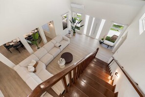 A spacious living area with a large sofa, a dining table, and a staircase leading to an upper floor.
