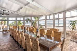 Enjoy meals in this dining area with a long table and wicker chairs, surrounded by a view of the beach and palm trees.