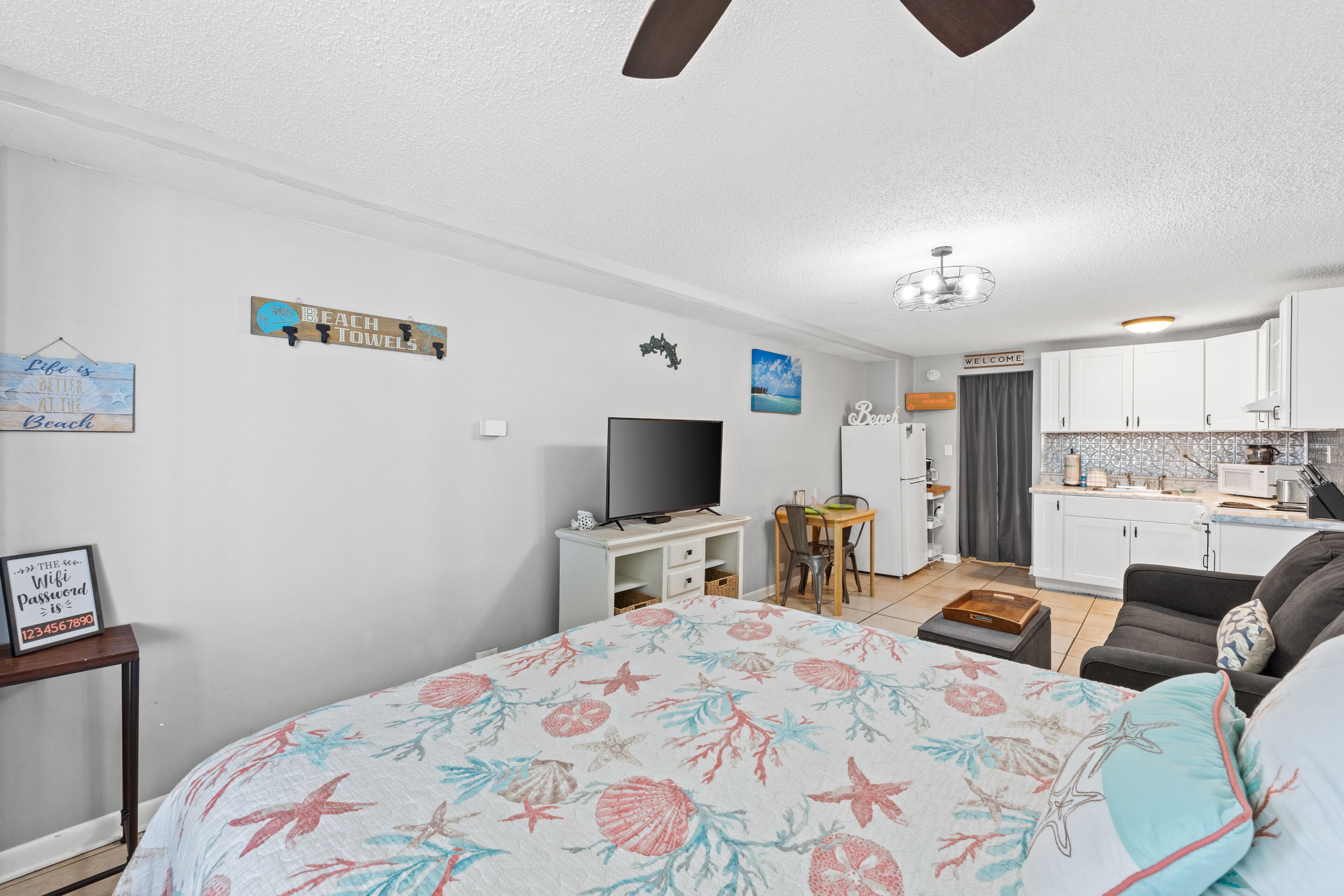 Un dormitorio con cama, televisor, escritorio y kitchenette.