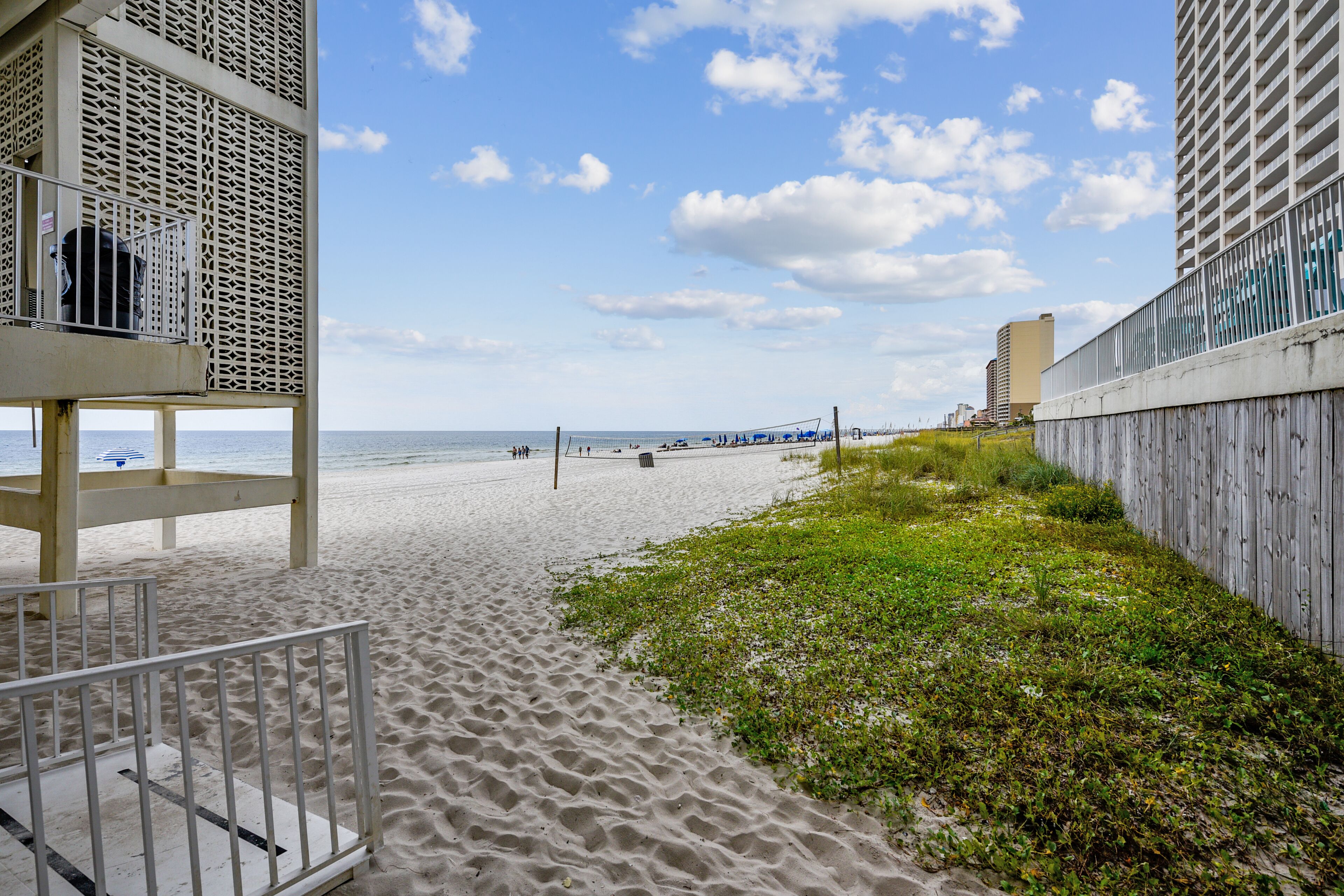 Ein Strand mit einer Holzlattenveranda, einem Rettungsturm und blauem Himmel.
