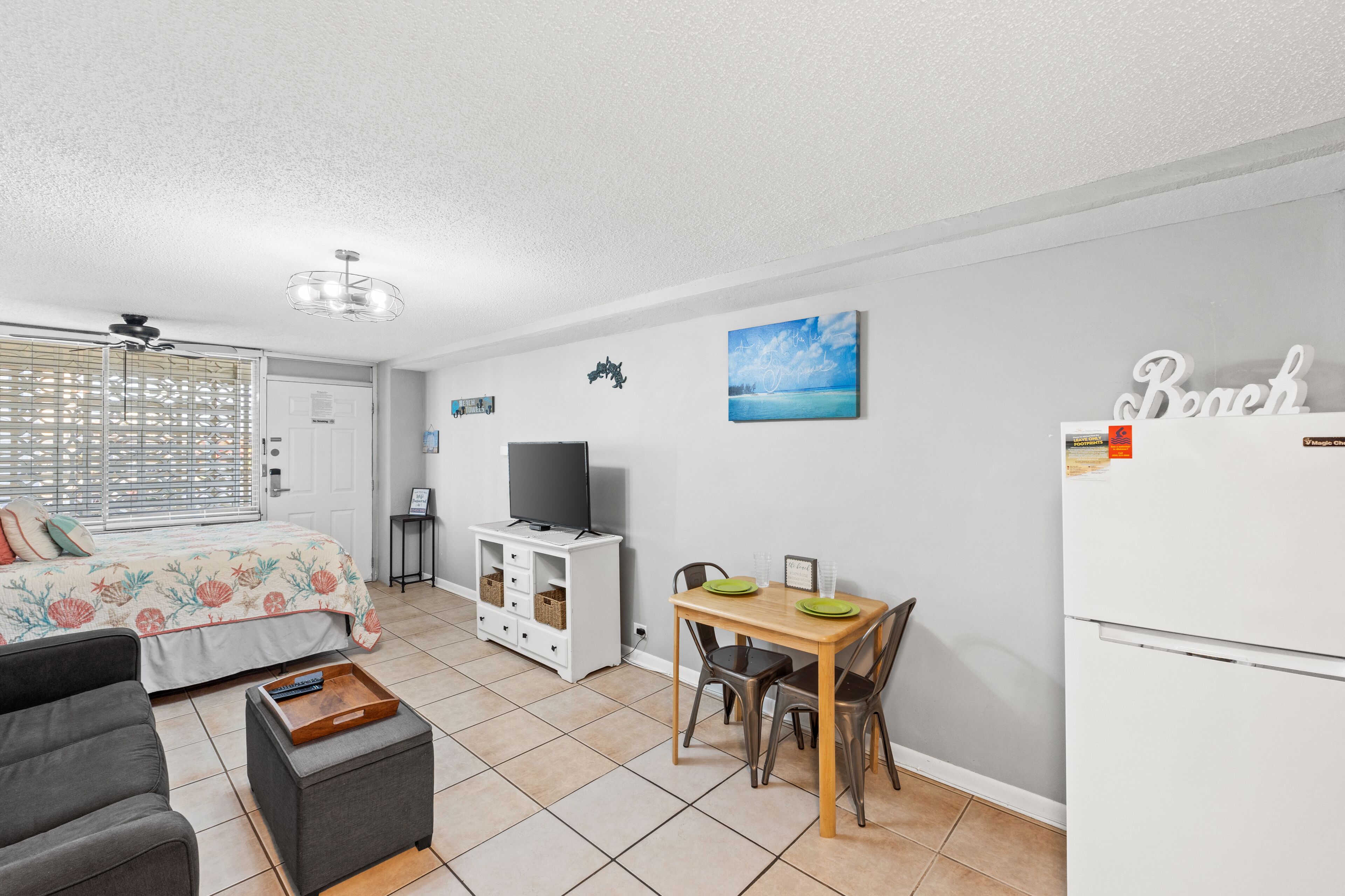 Ein kompakter Wohnraum mit Bett, Sofa, Esstisch mit Stühlen, Fernseher und Kühlschrank.
