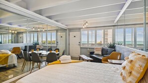 Hotellihuone, jossa on suuri sänky, ruokailutila, oleskelualue, josta on näkymä, sekä parveke, jossa on kaide.
