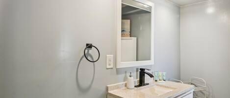 Un baño con un lavamanos blanco, un espejo y un perchero para toallas.