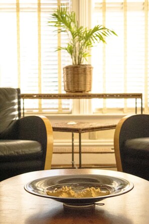 Une table à manger avec un saladier en verre au premier plan, une plante en osier sur une table à l’arrière-plan, et deux fauteuils en cuir.