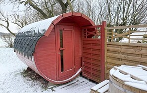 Ein rotes, gebogenes, einzelnes Gebäude mit Tür und kleinem Fenster, umgeben von Schnee und einem Holzzaun.