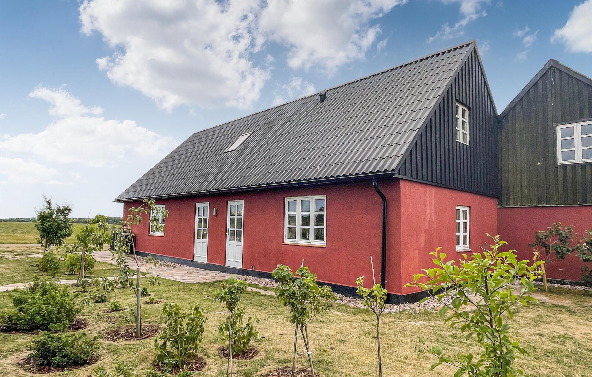 Ein rotes Haus mit dunklem Dach und weißen Fenstern, umgeben von einer Rasenfläche mit jungen Bäumen.