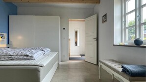 Un dormitorio con cama, una banca, una ventana y una puerta que da a otra habitación.