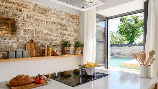 A modern kitchen with a stone wall, a large window, and a view of a swimming pool. - Awesome home in Tinjan (Tinjan)