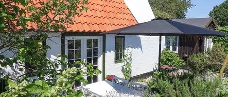 A white house with a red-tiled roof, a black umbrella, and a garden with lavender plants.
