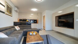 Una sala de estar moderna con un sofá seccional gris, una mesa de centro de madera y un televisor grande montado en la pared.