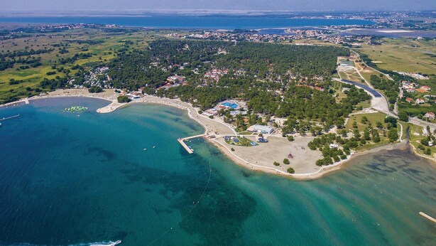 Vista aérea de un pueblo costero con un puerto deportivo, playas de arena y una combinación de edificios residenciales y comerciales.