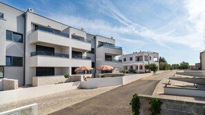 Un edificio residencial moderno con balcones, un camino pavimentado y mobiliario exterior con sombrillas.