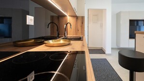 Una cocina moderna con encimera de madera, dos lavamanos dorados, una estufa negra y una campana extractora negra.
