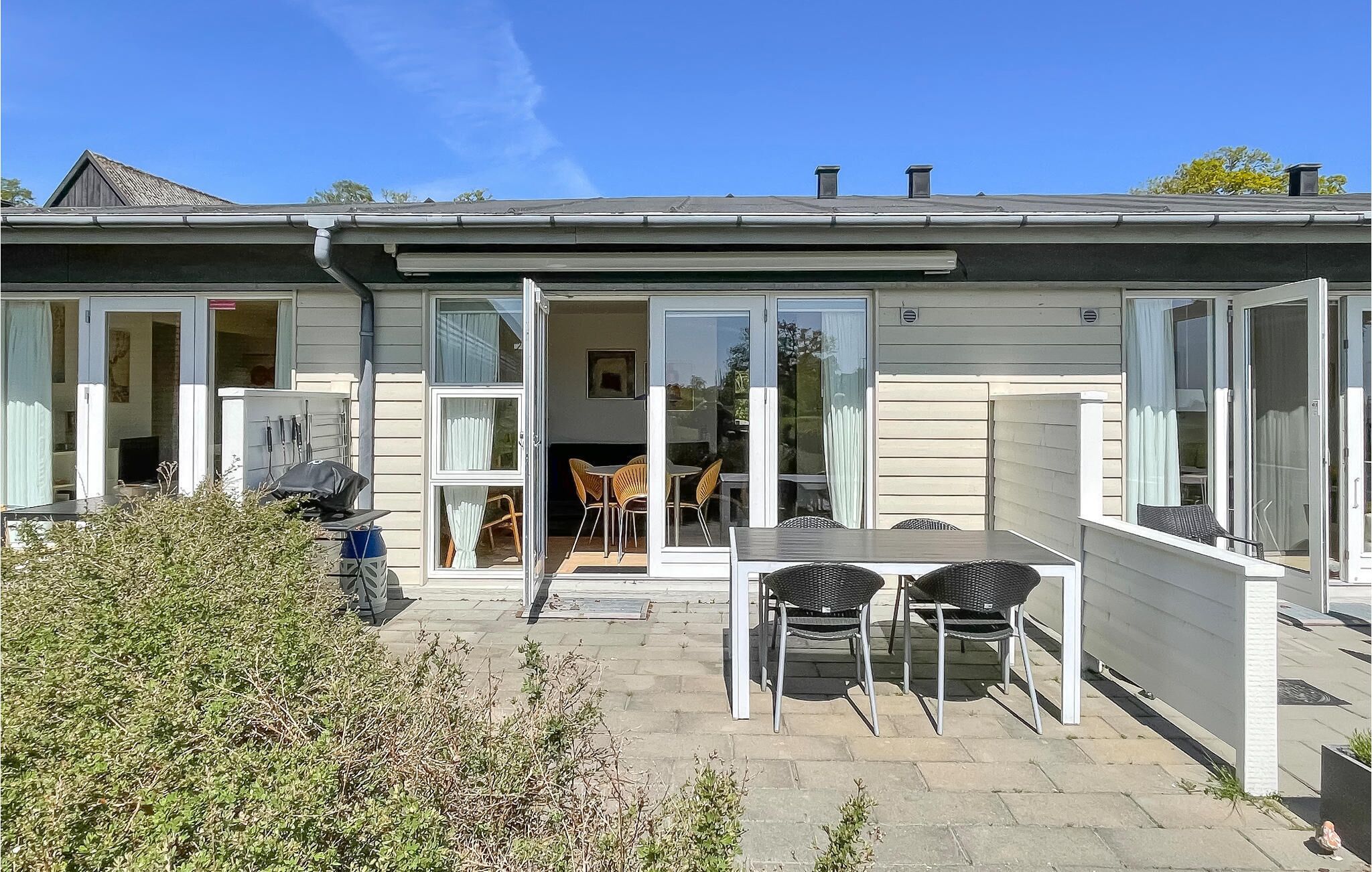 A modern house with a patio area featuring a table and chairs, a sliding glass door leading to an interior room, and a small garden area.