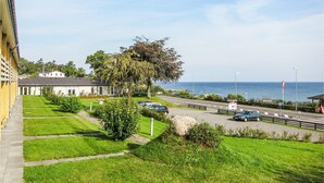 A coastal road with a view of the sea, a row of parked cars, and a building with a grey roof. - Awesome apartment in Allinge (Allinge)