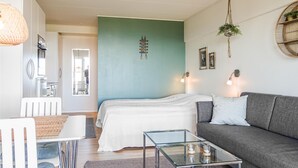 A modern living room with a bed, a glass coffee table, a grey sofa, and a dining area with a white table and chairs. - Awesome apartment in Allinge (Allinge)