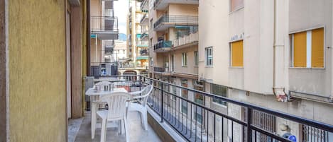 A narrow balcony with a table and chairs, surrounded by multi-story buildings with balconies and windows.