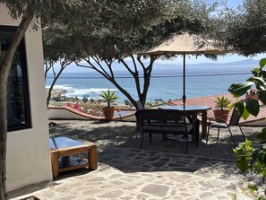 Eine Terrasse mit Tisch und Stühlen unter einem Sonnenschirm mit Blick auf das Meer.
