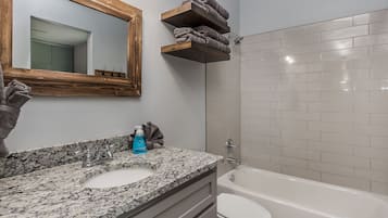 A bathroom with a granite countertop sink, a mirror with a wooden frame, a towel rack, a toilet, and a bathtub.
