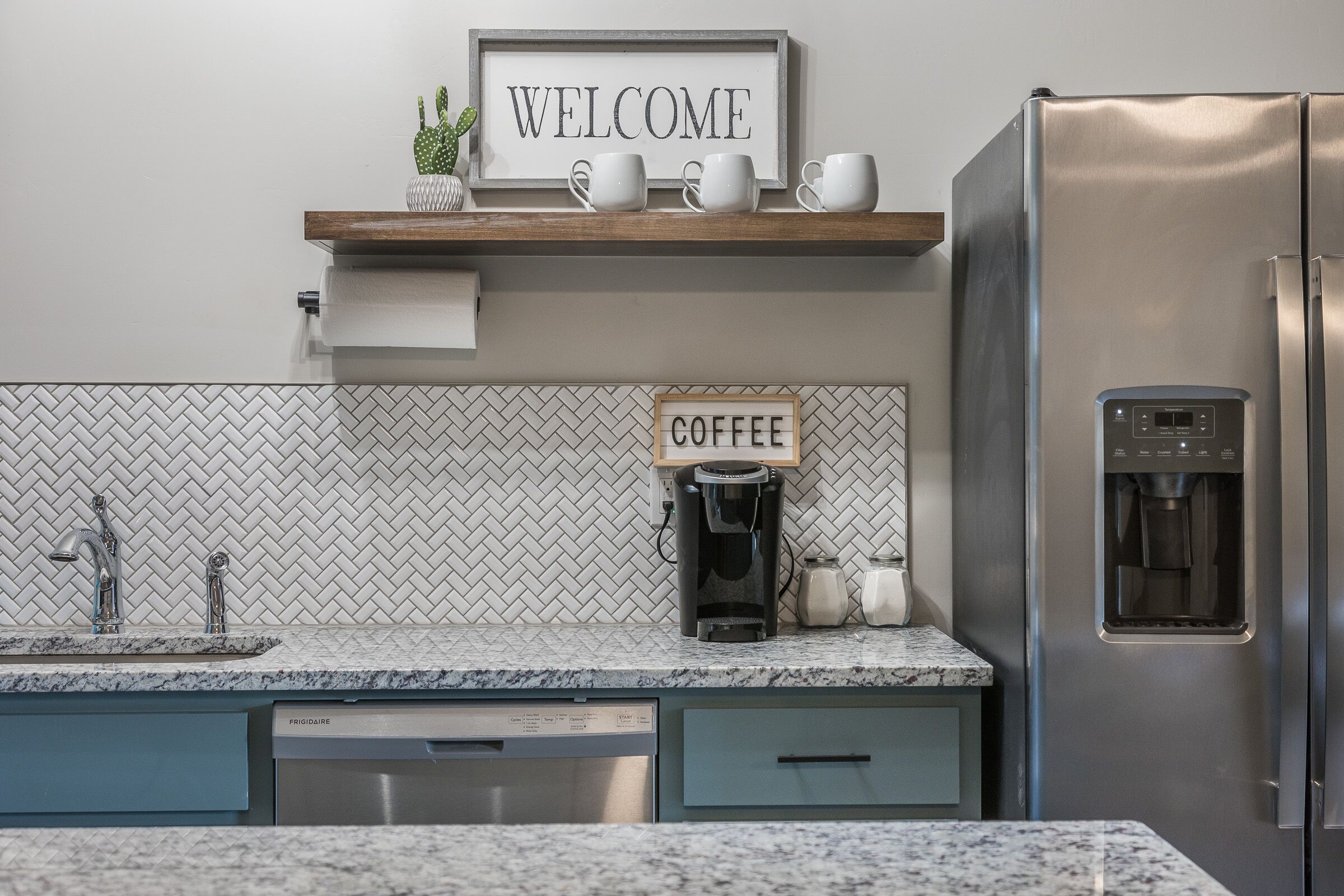 Een moderne keuken met een koffiehoek, een roestvrijstalen koelkast en een backsplash van visgraatmozaïek.