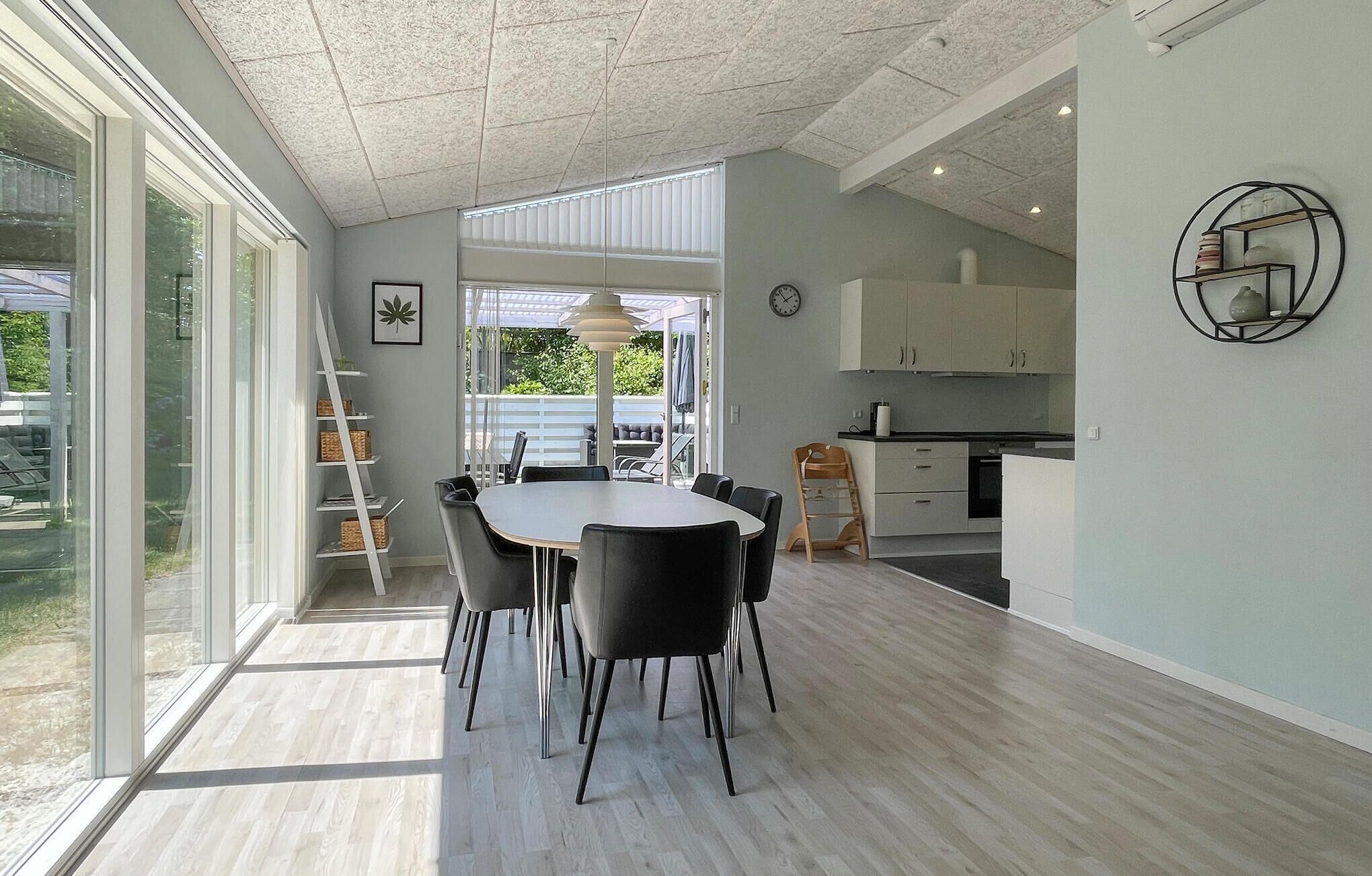 Une cuisine moderne avec des meubles blancs, un coin repas doté d’une table ronde et de chaises, et une vue sur une terrasse extérieure, visible à travers de grandes fenêtres.