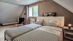 A bedroom with two beds, a chair, a nightstand, a window, and a painting on the wall. - 3 bedroom awesome home in Moelan sur Mer (Moelan sur Mer)