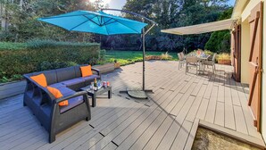 An outdoor patio with a black sofa, orange cushions, a round table, and a blue umbrella. - 3 bedroom awesome home in Moelan sur Mer (Moelan sur Mer)