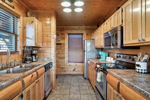 A wooden cabin kitchen with granite countertops, stainless steel appliances, and wooden cabinets.