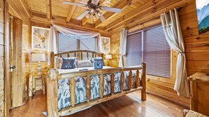 A wooden cabin bedroom with a bed, wooden headboard, ceiling fan, and windows with curtains. - ❤ Amazing Views⛰ Hot Tub✦ Game Rm♜ Theater📽 3 King Beds (Sevierville)