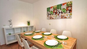 Comedor con una mesa de madera dispuesta para cuatro personas, sillas blancas y un mantel corrido verde.